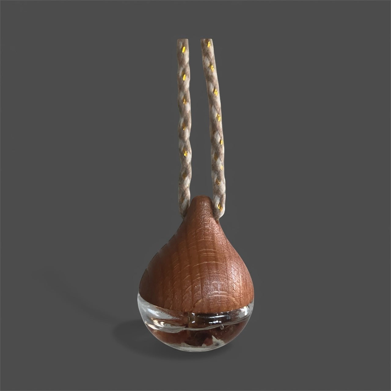 COCO MELTS & CO teardrop car hanging diffuser with wooden top and glass base filled with liquid and botanicals, suspended by a braided rope.